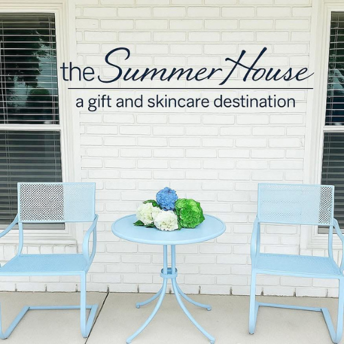 The Summer House exterior with a white wall, baby blue chairs and a blue and green bouquet on the table