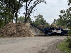 Large pile of mulch and wood debris being processed by a mulcher after the June 2025 storm at McIntosh Woods State Park in Ventura, Iowa.